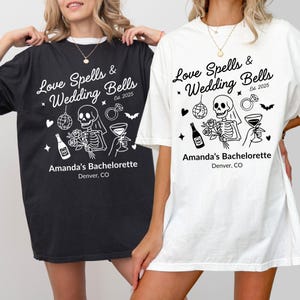 May include: Two t-shirts, one black and one white, with a bachelorette party design. The design includes the text "Love Spells & Wedding Bells Est. 2025" and illustrations of a skeleton, disco ball, and wedding symbols. The text "Amanda's Bachelorette Denver, CO" is also present.