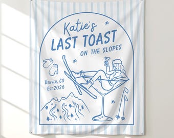 May include: Blue and white wall tapestry with a ski-themed illustration. The design features a woman in a martini glass, skis, mountains, and the text "Katie's Last Toast on the Slopes." Includes "Denver, CO Est. 2026."