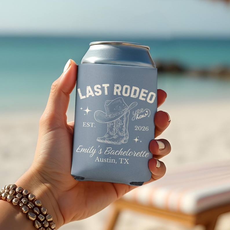 以下が含まれることがあります： 「Last Rodeo」の文字とカウボーイハットとブーツのグラフィックが描かれた、水色の缶クーラー。 「Emily's Bachelorette, Austin, TX」の文字も表示されています。 ビーチで人がクーラーを持っています。