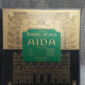 May include: A black and gold record album cover featuring a drawing of the Teatro alla Scala opera house in Milan, Italy. The album cover is for a recording of Giuseppe Verdi's opera Aida, featuring Maria Meneghini Callas, Richard Tucker, Fedora Barbieri, Tito Gobbi, Giuseppe Modesti, Nicola Zaccaria, Franco Ricciardi, and Elvira Galassi. The album is conducted by Tullio Serafin.