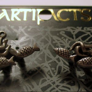 May include: A pair of silver earrings featuring a fish and anchor design. The earrings are on a card with the word "ARTIFACTS" printed on it.