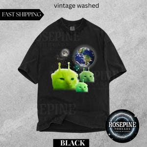 May include: Black t-shirt with a graphic featuring green alien cat faces, a planet Earth, and a moon. The shirt has the text "vintage washed" and "BLACK". The brand name "ROSEPINE THREADS" is also visible.