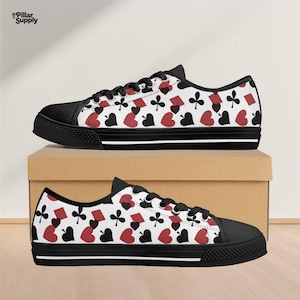 May include: Pair of canvas sneakers with a playing card suit pattern. The shoes have a white background with red hearts, black spades, clubs, and diamonds. The toe and sole are black with white stripes.