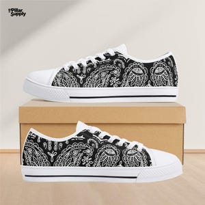 May include: White-soled canvas sneakers with a black paisley pattern. The shoes have white laces and a black stripe along the sole. The shoes are displayed on a cardboard box.