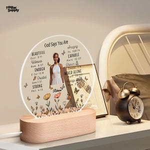May include: A decorative LED night light with a wooden base. The light features a circular design with the text "God Says You Are" and inspirational words. A photo of a woman is in the center, surrounded by butterflies and floral illustrations.