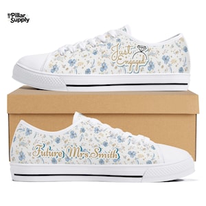 May include: White canvas sneakers with a floral pattern in blue and gold. One shoe says "Just Engaged" with a diamond ring graphic, and the other says "Future Mrs. Smith" in gold script. The shoes have white soles and black trim.