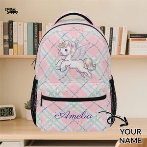 May include: Pink plaid backpack with a unicorn graphic. The backpack features a black handle, black mesh side pockets, and the name "Amelia" in cursive. The unicorn has a golden horn and rainbow-colored mane and tail.