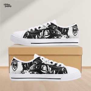 May include: White canvas sneakers with black and white leaf pattern. The low-top shoes feature white laces, a white rubber sole, and a black stripe. The Guam seal is on the outer side of the shoe.