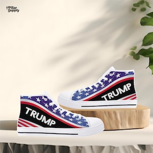 May include: Pair of high-top canvas sneakers with a patriotic design. The sneakers feature a white base, with a blue and white star pattern, red and white stripes, and the word "TRUMP" in bold white letters.