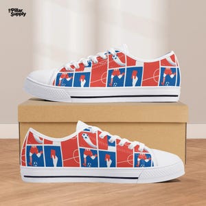 May include: White canvas sneakers with a red, white, and blue soccer-themed pattern. The design features soccer players, soccer balls, and red cards. The shoes have white laces and a black stripe along the sole.