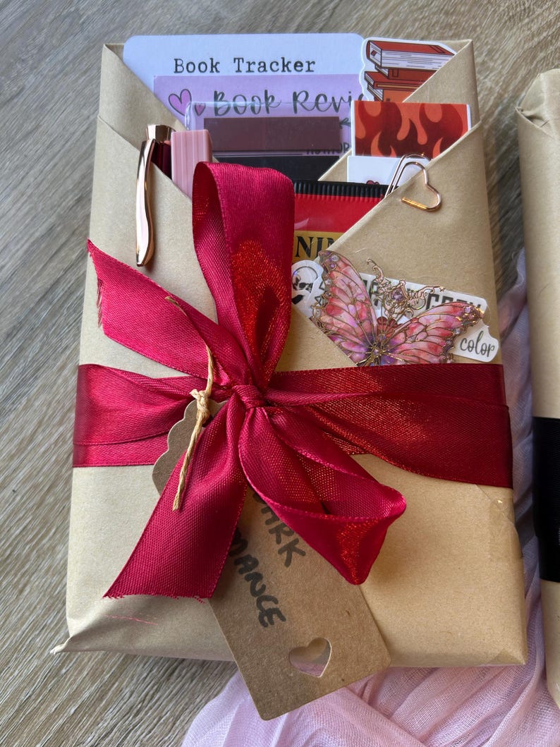 Op de afbeelding: Een cadeau verpakt in bruin papier, vastgebonden met een bordeauxrode lint en een label. Het pakket bevat een pen, stickers en een bladwijzer. Het label luidt "Dark Romance".