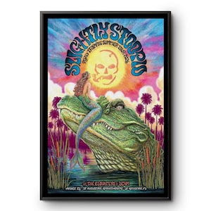 Könnte beinhalten: Ein gerahmtes Konzertplakat für die Slightly Stoopid Road Trippin Summer Tour 2026. Das Bild zeigt eine Meerjungfrau auf einem großen grünen Alligator in einem Sumpf mit Palmen, eine gelbe Sonne mit Totenkopf und Text für The Elovaters & Denm am unteren Rand.