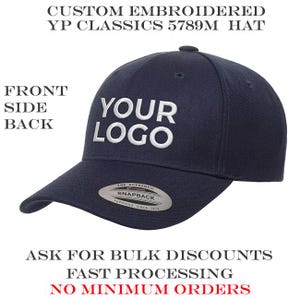 May include: A navy blue baseball cap with white embroidered text that says "YOUR LOGO". The cap has a curved brim and a snapback closure. The text "CUSTOM EMBROIDERED YP CLASSICS 5789M HAT" is at the top. The text "ASK FOR BULK DISCOUNTS FAST PROCESSING NO MINIMUM ORDERS" is at the bottom.