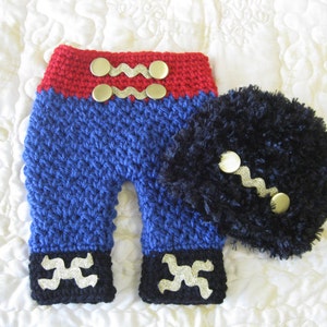 Puede incluir: Conjunto de beb&eacute; de ganchillo en rojo, azul y negro con botones dorados. El conjunto incluye pantalones y un gorro.