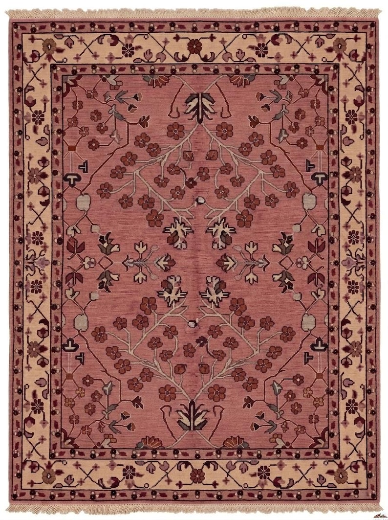 May include: A rectangular rug with a central field of dusty rose, adorned with floral and botanical patterns in shades of brown, beige, and green. The rug has a beige border with intricate designs and fringe.