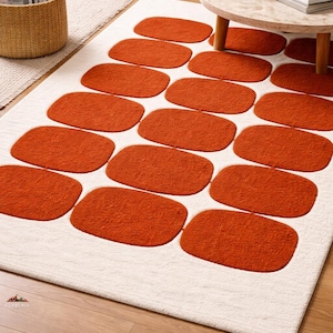Peut inclure: Tapis rectangulaire blanc orné de grands rectangles arrondis orange. Le tapis est posé sur un sol en bois. Une table basse et d'autres meubles sont visibles en arrière-plan. Design moderne.