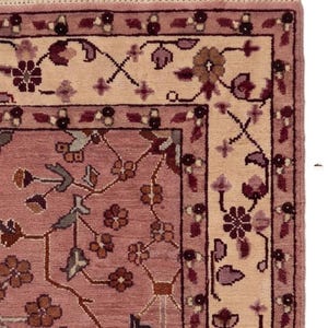 May include: Close-up of a section of a rug with a floral design. The rug features a dusty rose field with a cream-colored border. The border and field are adorned with floral and vine patterns in shades of burgundy, brown, and green.