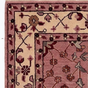 May include: Close-up of a section of a rectangular rug with a floral design. The rug features a light pink field with a cream-colored border and a darker pink border. The design includes floral and vine motifs in shades of pink, burgundy, and brown.