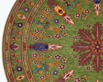 May include: A circular green rug with a detailed floral pattern. The rug has a central design and a border with repeating patterns in red, blue, yellow, and purple. The rug is made of a soft, woven material, suitable for a living space.