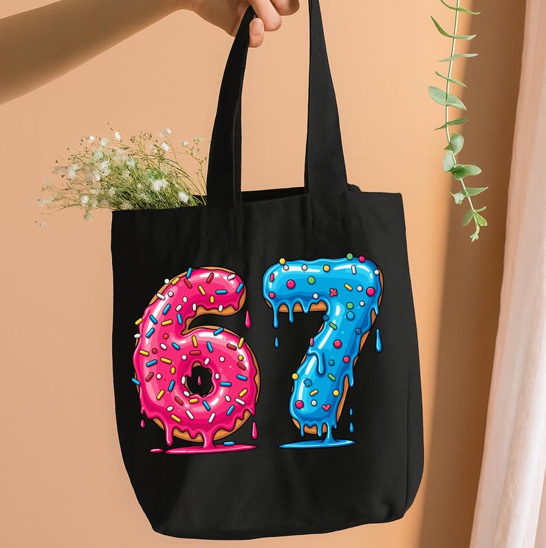 May include: Black tote bag with the numbers 6 and 7 designed as donuts. The number 6 is pink with sprinkles, and the number 7 is blue with sprinkles. The bag has black handles and is filled with white flowers.