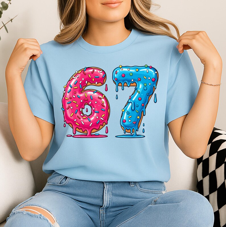 May include: A pale blue t-shirt with the number "67" in a donut design. The "6" is pink with pink sprinkles, and the "7" is blue with blue sprinkles. The donuts have a dripping icing effect.