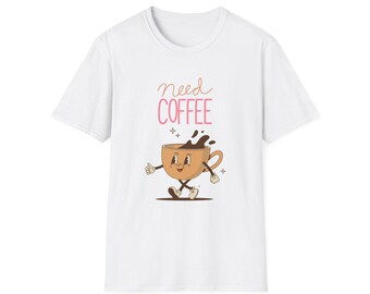 May include: White t-shirt featuring a cartoon coffee cup with a smiling face, arms, and legs. The cup has coffee spilling out and the words "need COFFEE" in pink script above it. The design is centered on the shirt.