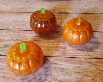 Puede incluir: Tres contenedores de color naranja en forma de calabaza con tallos verdes. Los contenedores están hechos de un material brillante y tienen una superficie ligeramente texturizada.