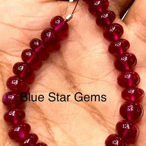 Könnte beinhalten: Eine Kette aus polierten, tiefroten Edelsteinperlen. Die Perlen sind auf einem dünnen Draht aufgefädelt, mit einem silberfarbenen Verschluss. Der Text "Blue Star Gems" ist im Bild zu sehen.