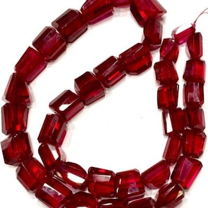 Può includere: Una collana di perline rettangolari sfaccettate di un rosso intenso. Le perline sono infilate insieme, mostrando le loro superfici lucide e le forme geometriche. Le perline sono probabilmente fatte di vetro o un materiale simile.