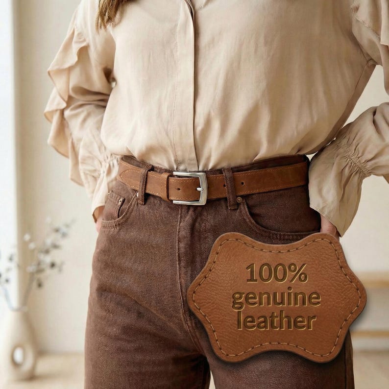 Pu&ograve; includere: Una cintura in pelle marrone con fibbia argentata &egrave; indossata con pantaloni marroni e una camicia beige abbottonata. Un'etichetta in pelle con la scritta "100% genuine leather" &egrave; visibile. La cintura &egrave; un accessorio classico.