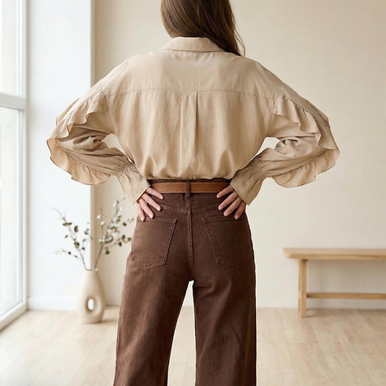 Pu&ograve; includere: Una camicia beige con maniche a balze e pantaloni marroni. La camicia ha un colletto classico e una vestibilit&agrave; rilassata. I pantaloni sono di colore marrone scuro e hanno una vita alta. Una cintura marrone &egrave; indossata con i pantaloni.