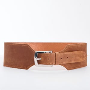 May include: A wide, brown leather belt with a silver-colored buckle. The belt has a suede-like texture and a rectangular shape. The buckle is a classic design, and the belt appears to be new.