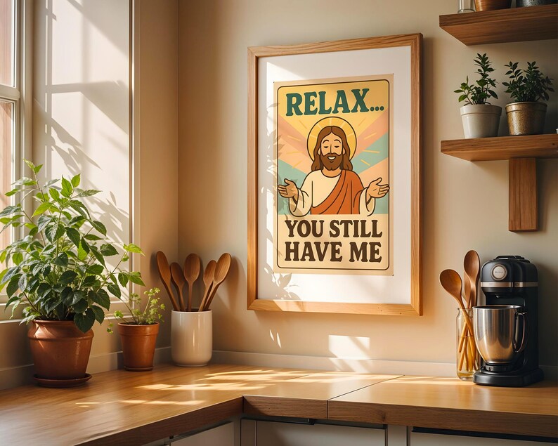 May include: A framed poster with the text "RELAX... YOU STILL HAVE ME" and an illustration of Jesus. The poster is in a wooden frame and hangs on a wall above a wooden countertop. The kitchen has plants and wooden utensils.