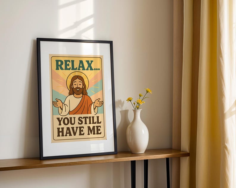 May include: Framed art print featuring a retro-style illustration of Jesus with a halo, arms outstretched. The text reads "RELAX... YOU STILL HAVE ME" in a vintage font. The artwork is in a black frame, displayed on a wooden shelf.