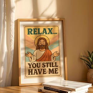 May include: Framed poster with a retro design featuring an illustration of Jesus with a halo, arms outstretched. The text reads "RELAX... YOU STILL HAVE ME" in a vintage font, set against a backdrop of pastel colors. The frame is made of light-colored wood.