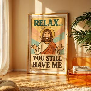 May include: A framed poster with the text "RELAX... YOU STILL HAVE ME" and an illustration of Jesus with a halo. The poster has a retro design with a beige background and a wooden frame. The image is in a well-lit room with a plant and a small table.