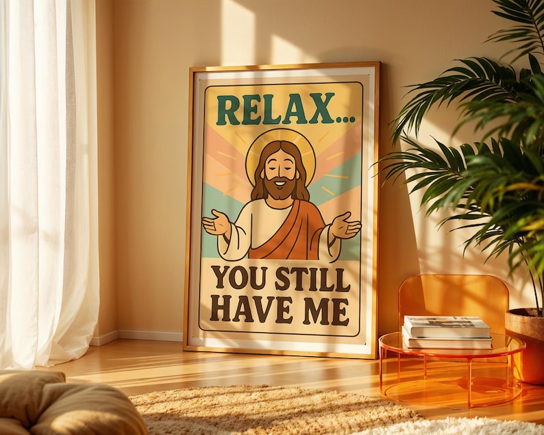 May include: A framed poster with the text "RELAX... YOU STILL HAVE ME" and an illustration of Jesus with a halo. The poster has a retro design with a beige background and a wooden frame. The image is in a well-lit room with a plant and a small table.