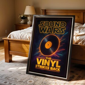 以下が含まれることがあります： 「SOUND WARS」と「THE VINYL STRIKES BACK」の黄色い文字と黒いレコード盤のグラフィックが描かれた額入りのポスター。ポスターは黒いフレームに入っており、ベッドと木製家具のある寝室の背景に配置されています。