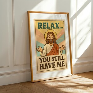 May include: Framed poster with a vintage design. The poster features an illustration of Jesus with the text "RELAX... YOU STILL HAVE ME" in a retro font. The artwork is in a wooden frame, leaning against a white wall.