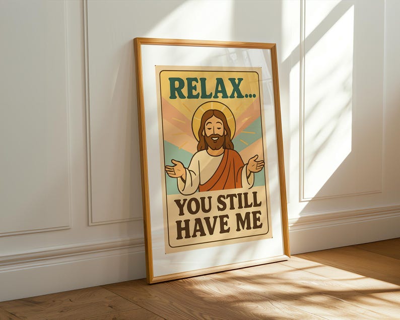 May include: Framed poster with a vintage design. The poster features an illustration of Jesus with the text "RELAX... YOU STILL HAVE ME" in a retro font. The artwork is in a wooden frame, leaning against a white wall.