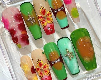 May include: A set of ten press-on nails featuring varied designs including red and white marble patterns, green and orange gradients, 3D yellow and red floral accents, metallic star charms, clear rhinestones, and raised translucent water droplets.