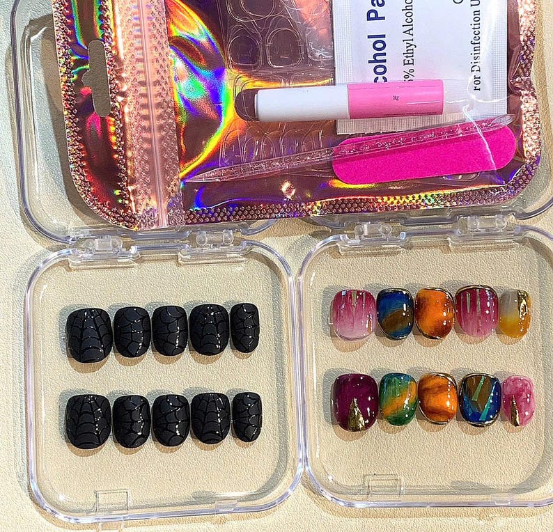 Puede incluir: Un juego de u&ntilde;as postizas en una caja de pl&aacute;stico transparente. Las u&ntilde;as presentan varios dise&ntilde;os, incluyendo patrones de telara&ntilde;a negros y arte abstracto colorido. Tambi&eacute;n se incluyen pegamento para u&ntilde;as y una lima de u&ntilde;as rosa.