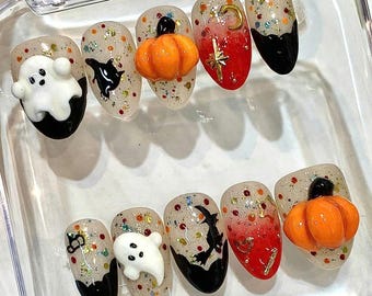 May include: A set of ten press-on nails featuring Halloween designs. The nails have a clear base with multicolored glitter, black tips, and 3D accents including white ghosts, orange pumpkins, black cats, and gold-toned star and moon charms.