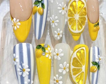 Puede incluir: Una colección de diez uñas artificiales con varios diseños. Algunas uñas presentan una base amarilla con acentos de margaritas blancas, mientras que otras muestran rodajas de limón o diseños de limón y hojas. Las uñas tienen un acabado brillante.
