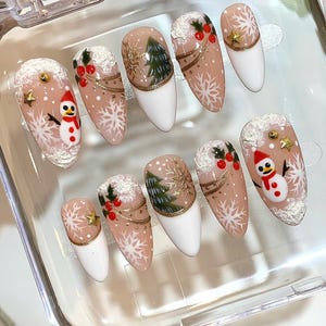 Könnte beinhalten: Ein Set aus zehn künstlichen Nägeln mit Weihnachtsmotiv. Jeder Nagel hat eine weiße Spitze, eine nude Basis und festliche Designs wie Schneeflocken, einen Schneemann, einen Weihnachtsbaum und Stechbeeren. Goldakzente und Glitzer sorgen für Glanz.