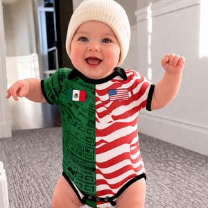 May include: A smiling baby wearing a white beanie and a unique onesie. The onesie is split down the middle, with the left side featuring the Mexican flag and the right side displaying the American flag. The outfit is trimmed in black.