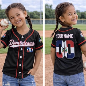 Könnte beinhalten: Schwarzes Baseball-Trikot mit roten und weißen Akzenten, mit dem Wort "Dominicana" und den Farben der Flagge der Dominikanischen Republik. Getragen mit Jeansshorts. Ein Baseball wird in der Hand gehalten.
