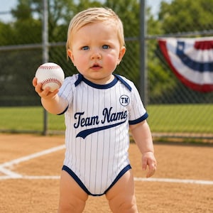 May include: A white baseball-style bodysuit with thin vertical navy blue pinstripes, navy blue trim, and the text "Team Name" in navy blue script across the chest, with a circular "TN" logo, paired with white sneakers and white socks.