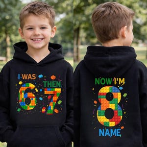 May include: Black hooded sweatshirt with colorful block-style numbers and text. The front says "I WAS 6-7 THEN." The back says "NOW I'M 8 NAME." The design features bright colors and a playful font, suitable for a child's birthday.