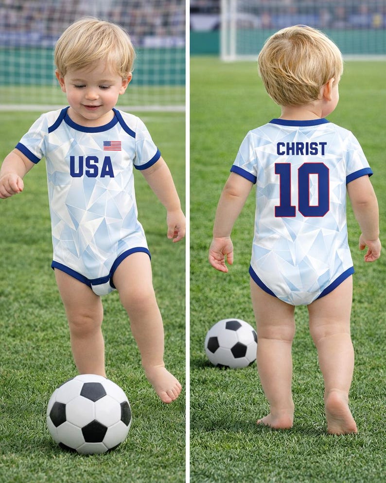 Puede incluir: Un beb&eacute; con un body de f&uacute;tbol azul claro y blanco con el texto "USA" y una bandera americana en la parte delantera. La parte trasera del body tiene el nombre "CHRIST" y el n&uacute;mero "10". El beb&eacute; est&aacute; de pie en un campo verde con un bal&oacute;n de f&uacute;tbol.